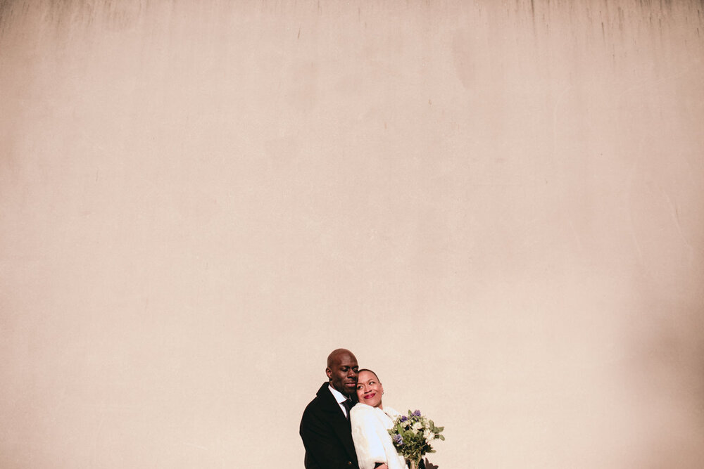  Black couple embracing on wedding day in front of concrete wall at the Virginia MFA in Richmond, VA, photo by Carly Romeo + CO. 