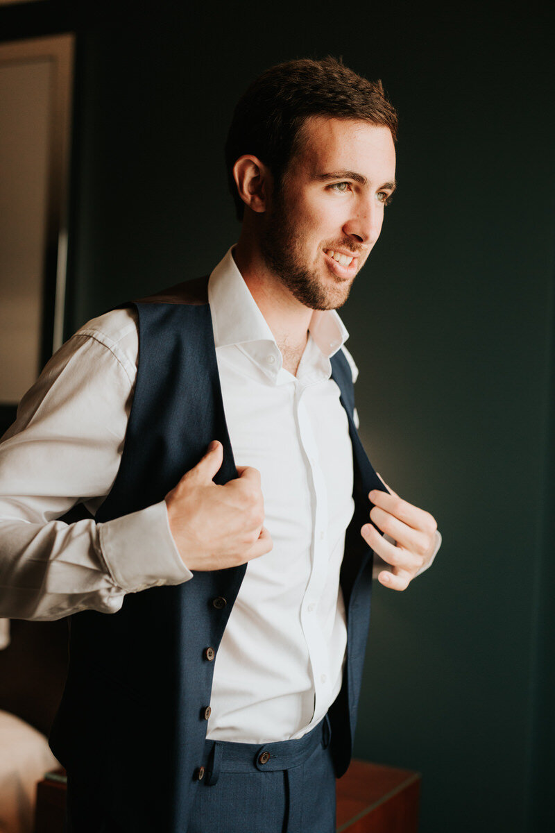 Groom putting on vest before wedding in Richmond Virginia Carly Romeo