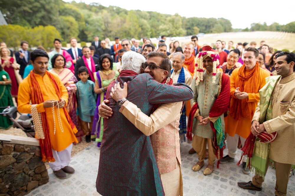 Fathers of bride and groom embrace in Indian Milni ceremony at Dover Hall Richmond Va Carly Romeo photography