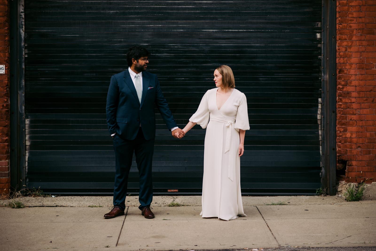 Newlywed mixed-race couple holding hands before black garage Pittsburgh PA Carly Romeo