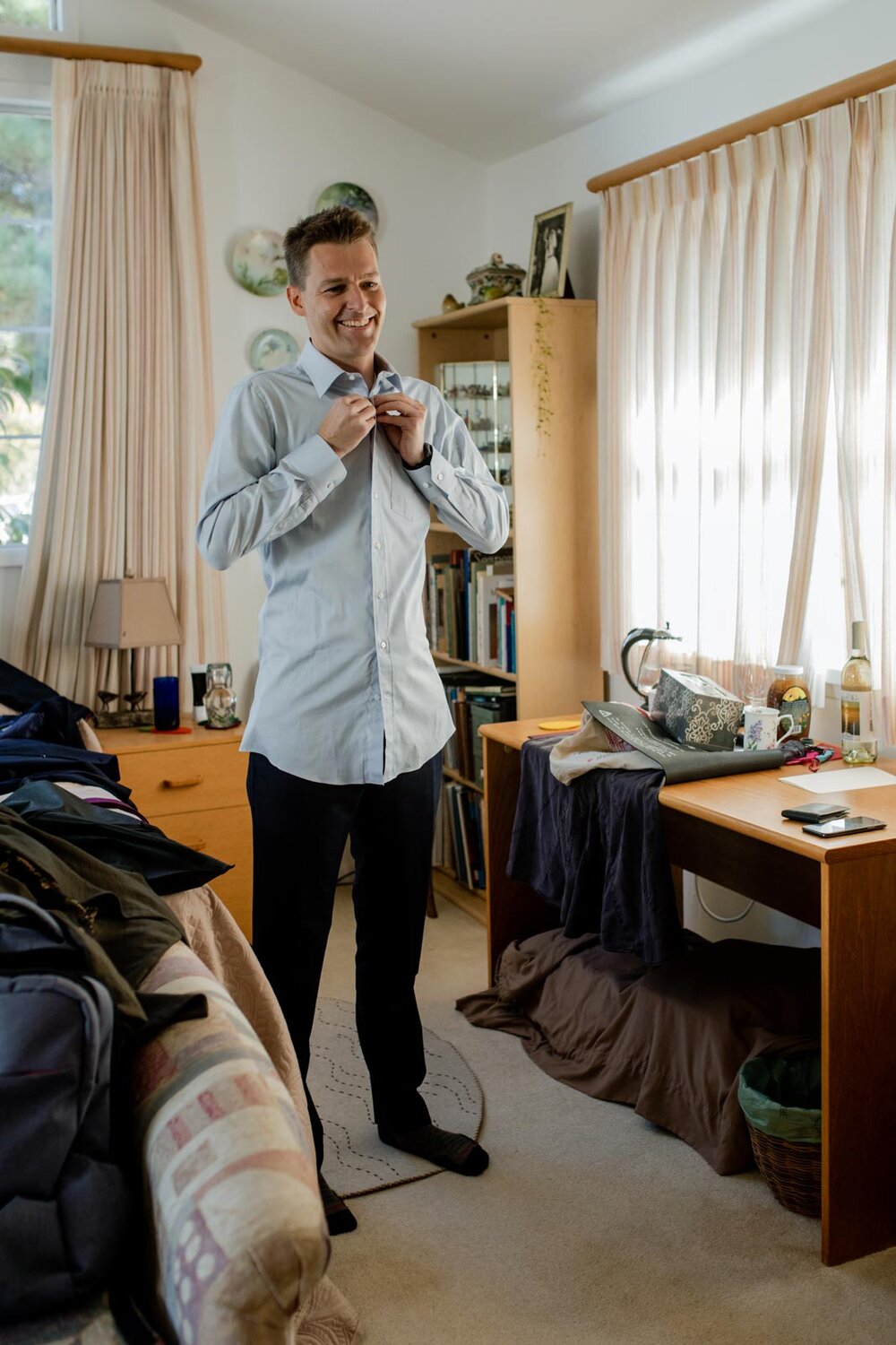 Groom buttoning up dress shirt in bedroom in Mendocino CA Carly Romeo feminist photography