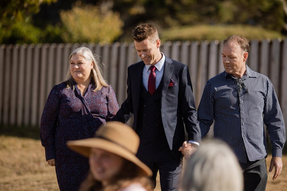 Groom walking to wedding ceremony with both parents in Mendocino CA Carly Romeo + Co.