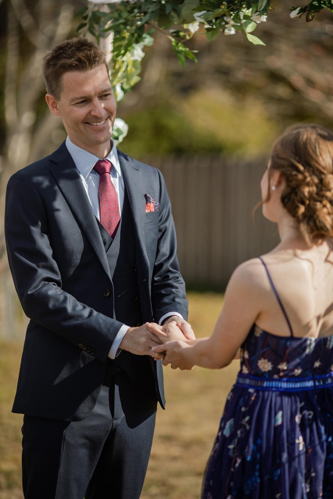 Groom smiling and holding brides hands under backyard chuppah in Mendocino CA Carly Romeo