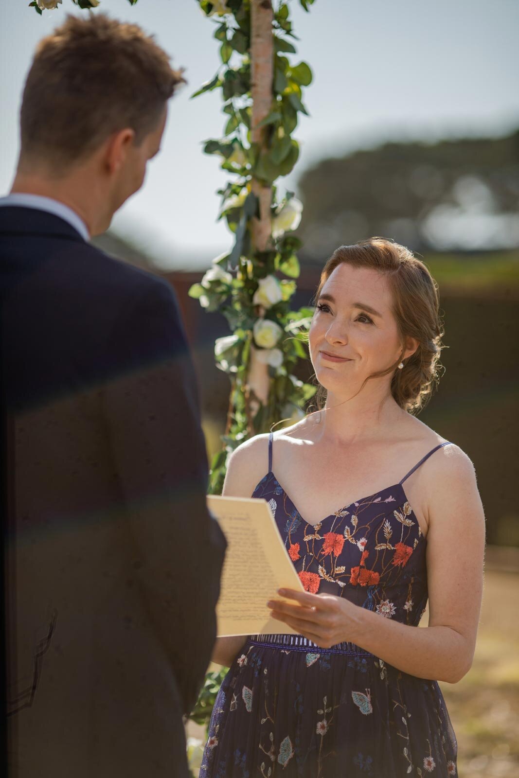 Bride in blue embroidered dress smiling up at groom with vows in Mendocino CA Carly Romeo and Co.