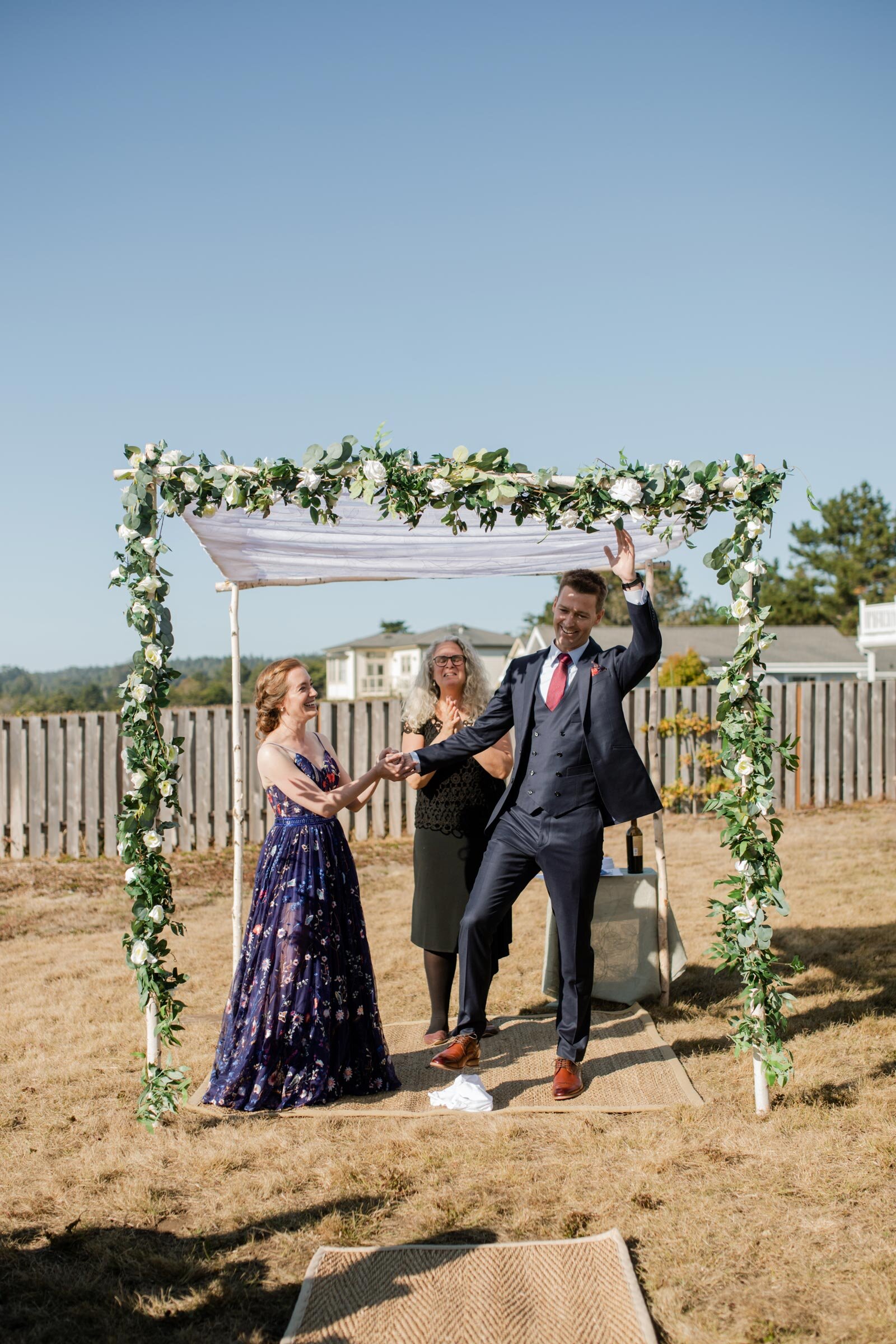 Groom after breaking the glass waving with bride and officiant in Mendocino CA Carly Romeo photography