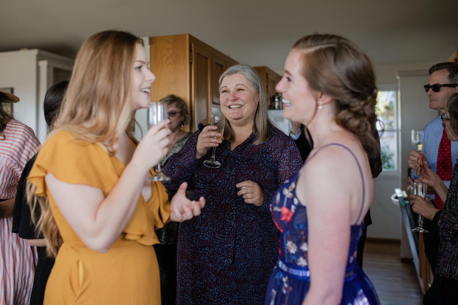 Bride smiling with two wedding guests drinking champagne in private residence in Mendocino CA Carly Romeo + Co.