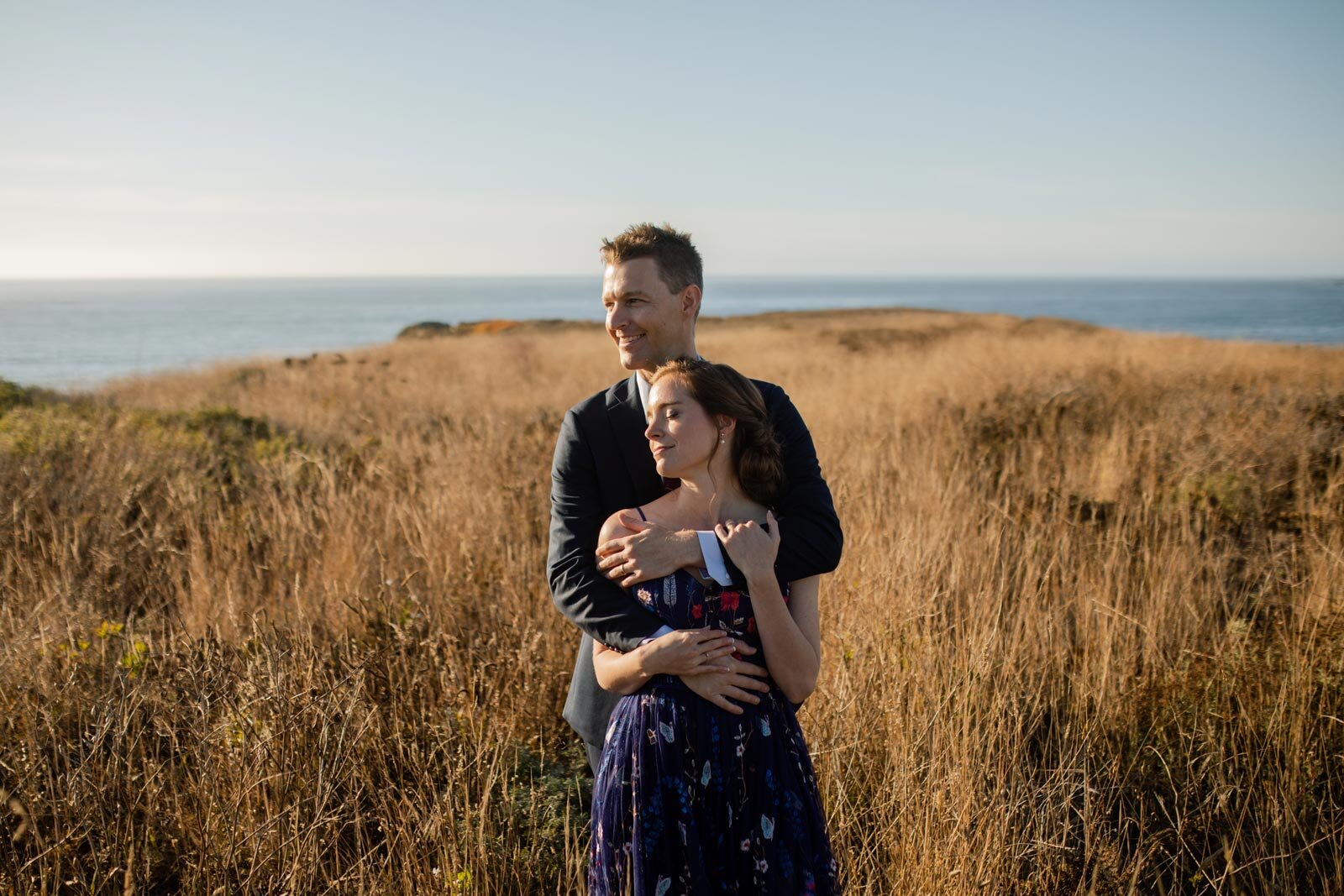 Groom holding bride on a grassy cliff overlooking the ocean in Mendocino CA Carly Romeo and Co