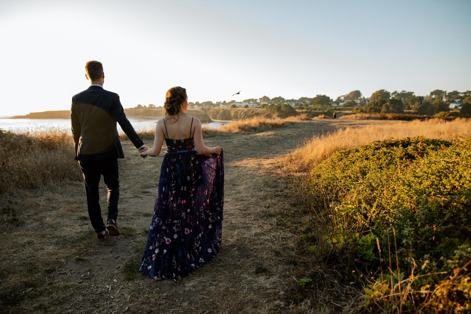 Newlywed couple walking hand in hand down dirt path overlooking the ocean in Mendocino CA Carly Romeo + Co