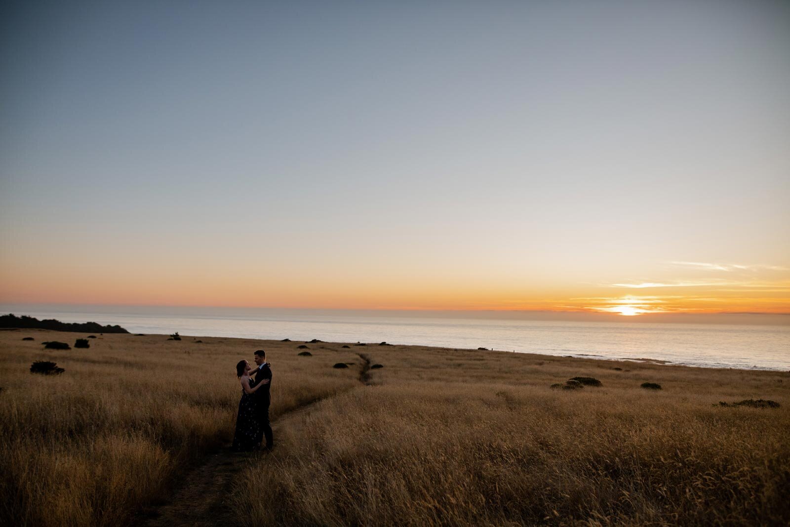 Newlywed couple embracing in grassy field before the sun setting into the ocean in Mendocino CA Carly Romeo