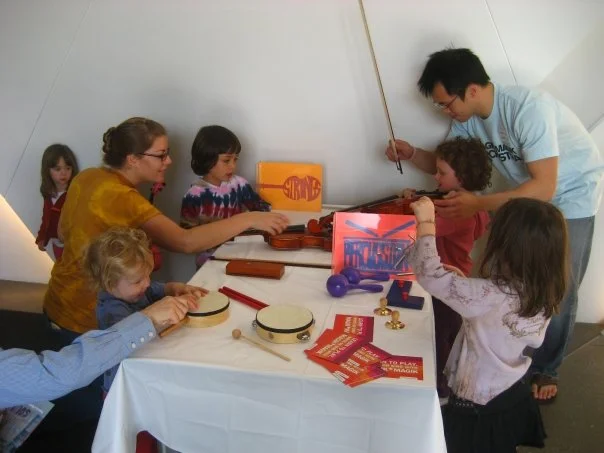 Lucas and Anna teach visitors to play the string instruments