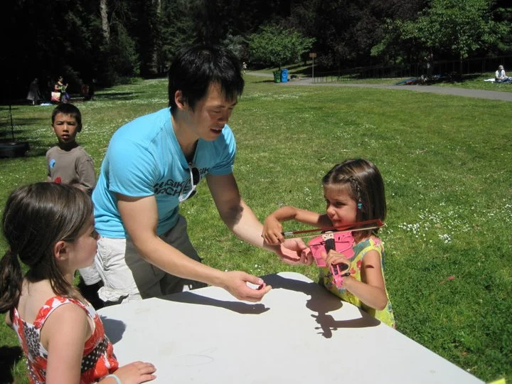 Lucas shows a young visitor how to play violin on a pink instrument just her size.
