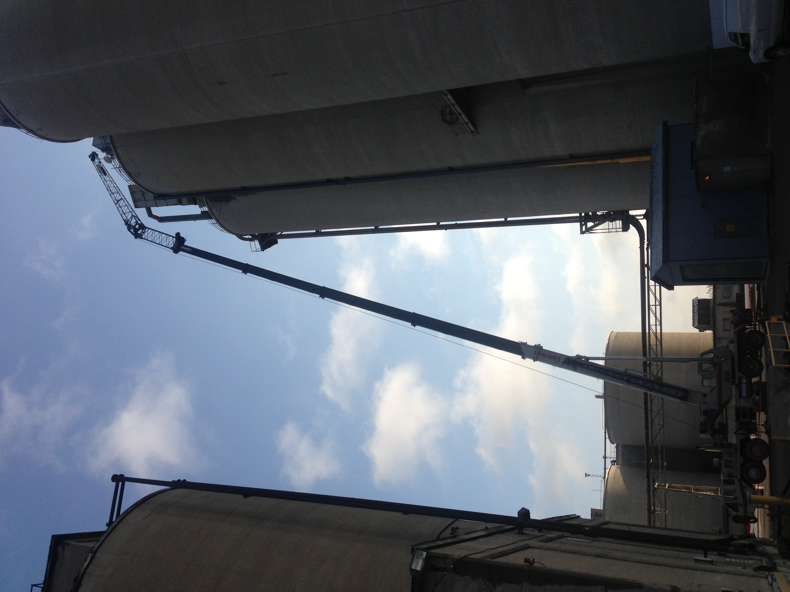 Mobile crane hoisting steel pipe on silo roof on farm