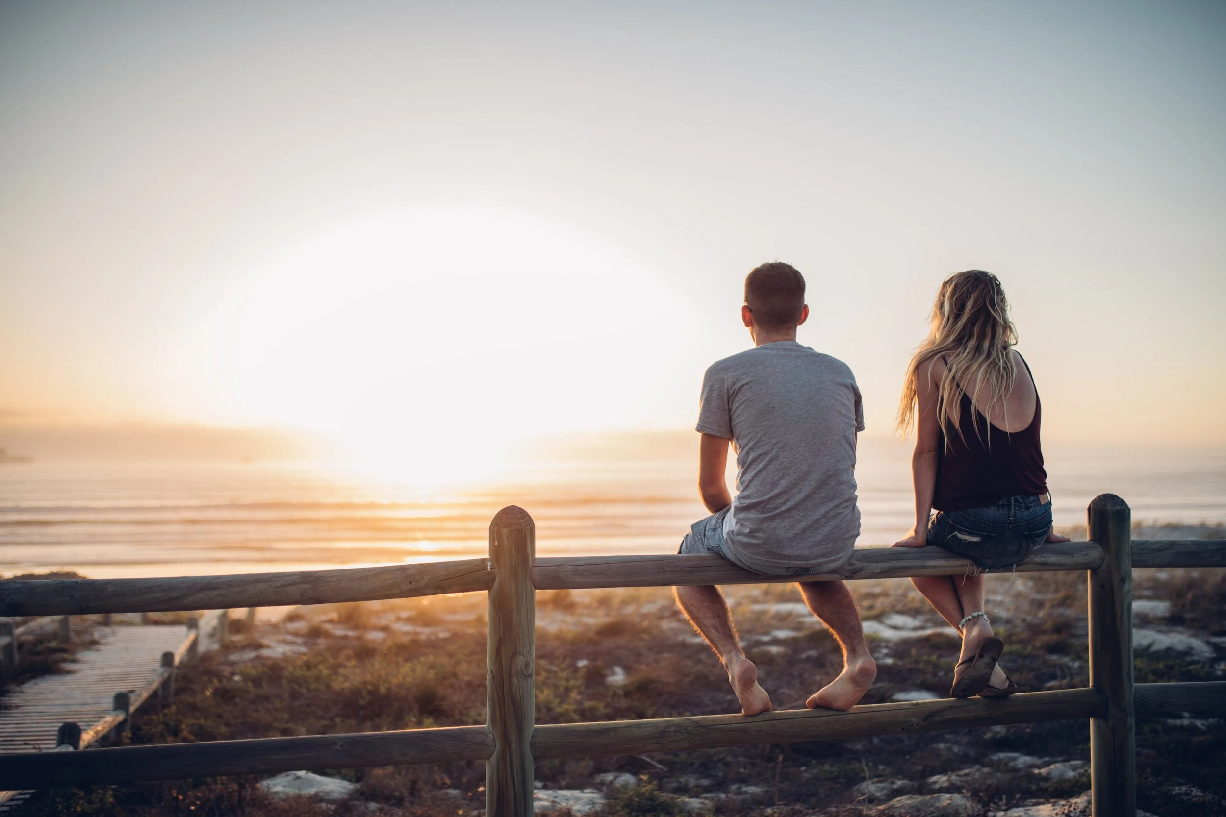 rear-view-couple-sitting-railing-against-beach.jpg