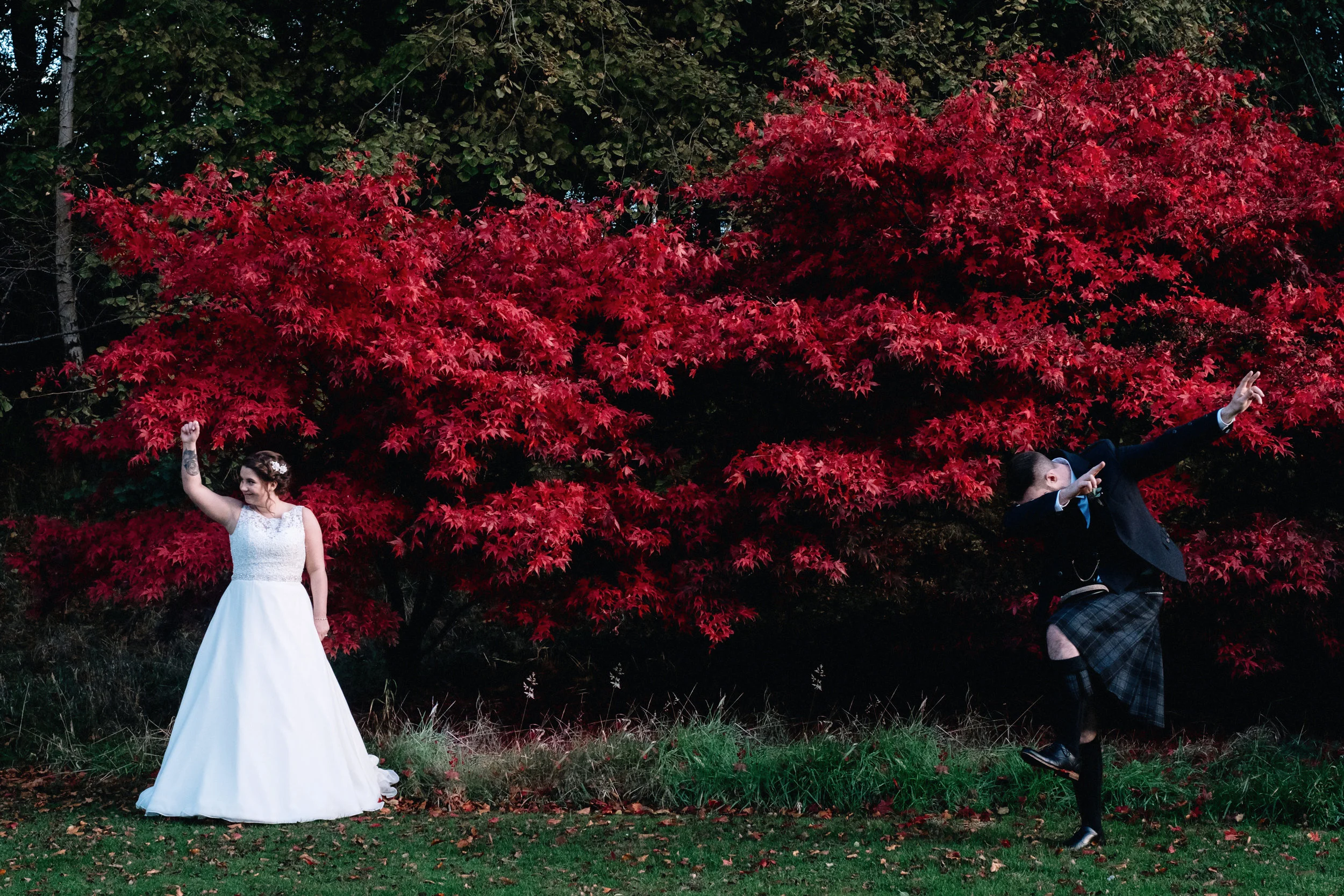 Bride and groom hold a dance move in front of a red bush