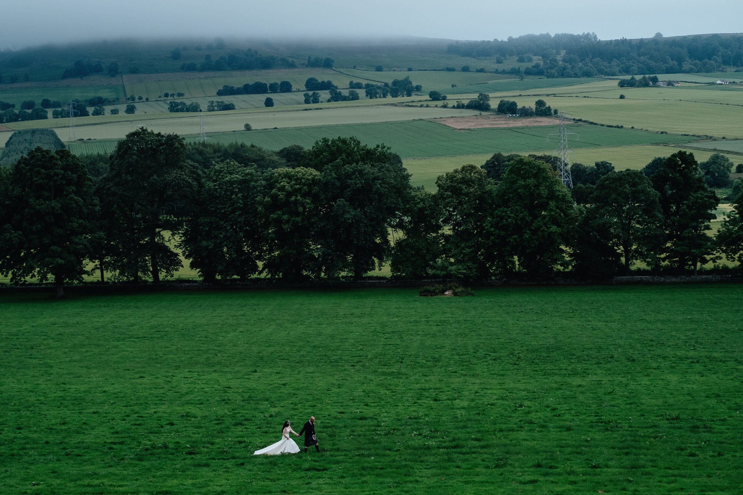Bride and groom walk in field holding hands
