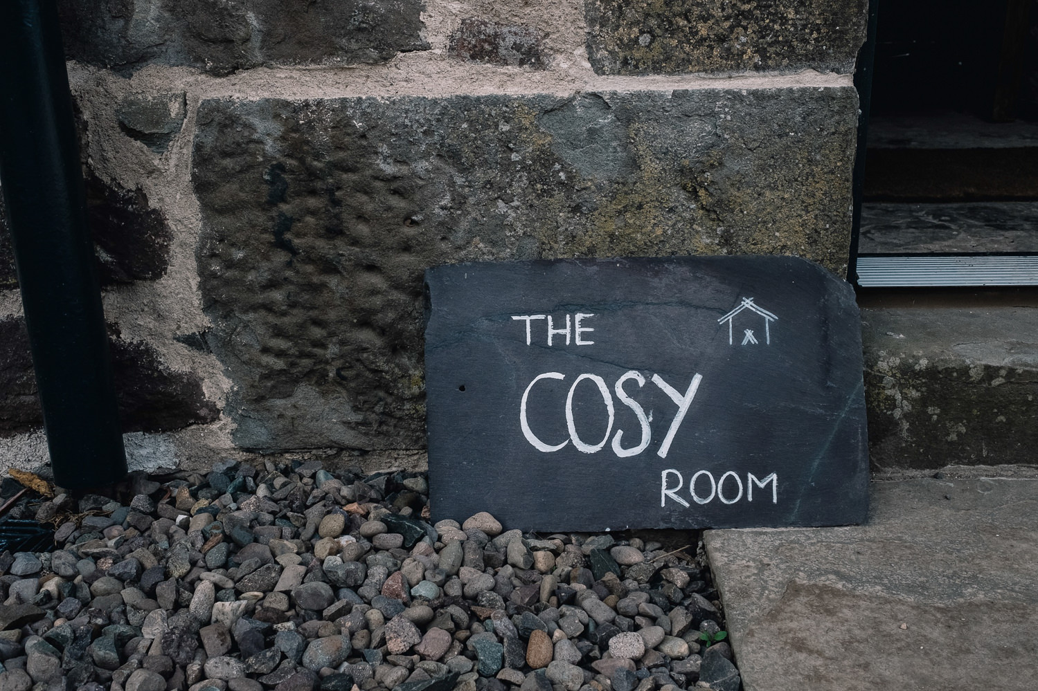 Slate with name and branding logo of the Cosy Room ll sits on the ground.