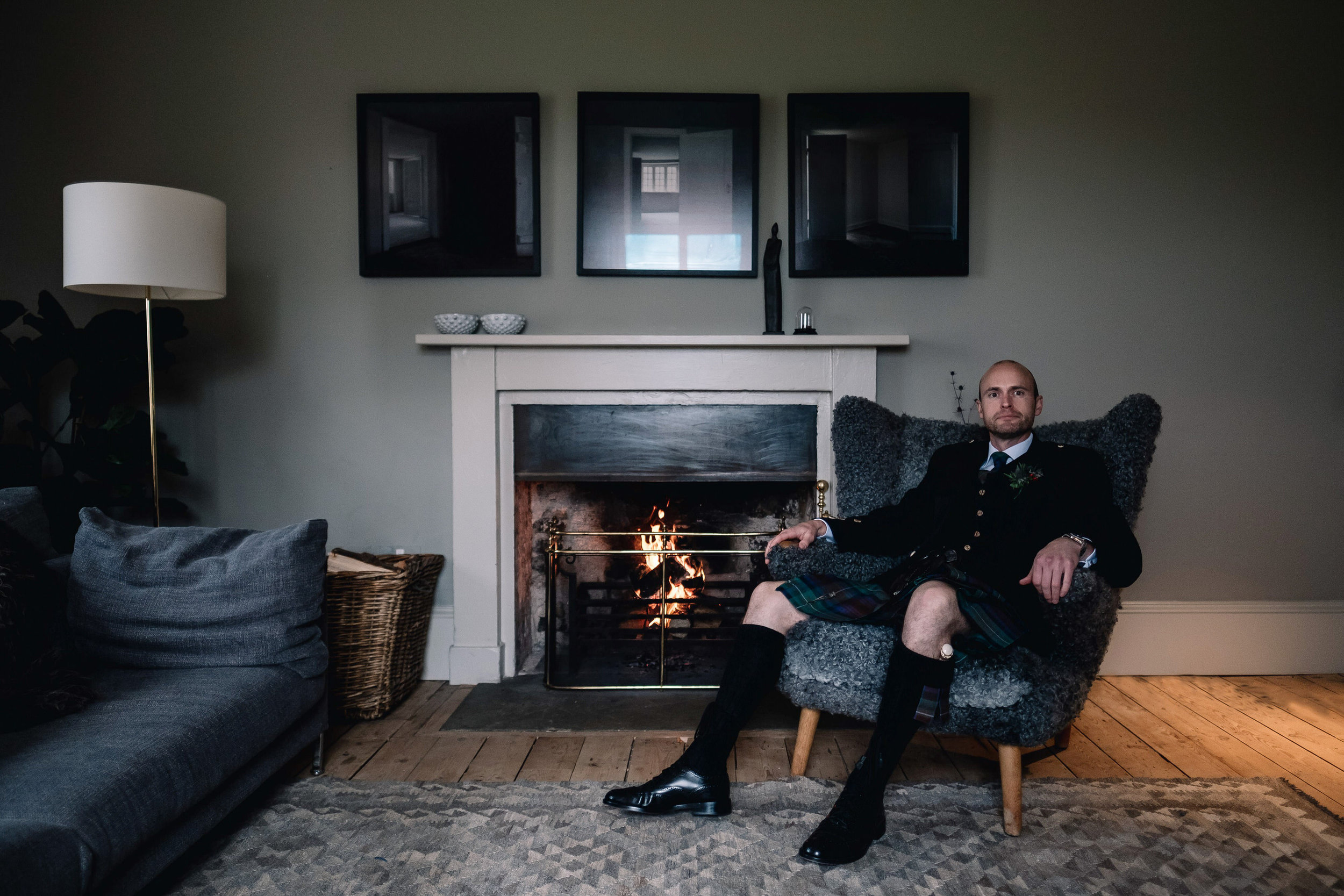  Portriat of groom sitting by log fire. 