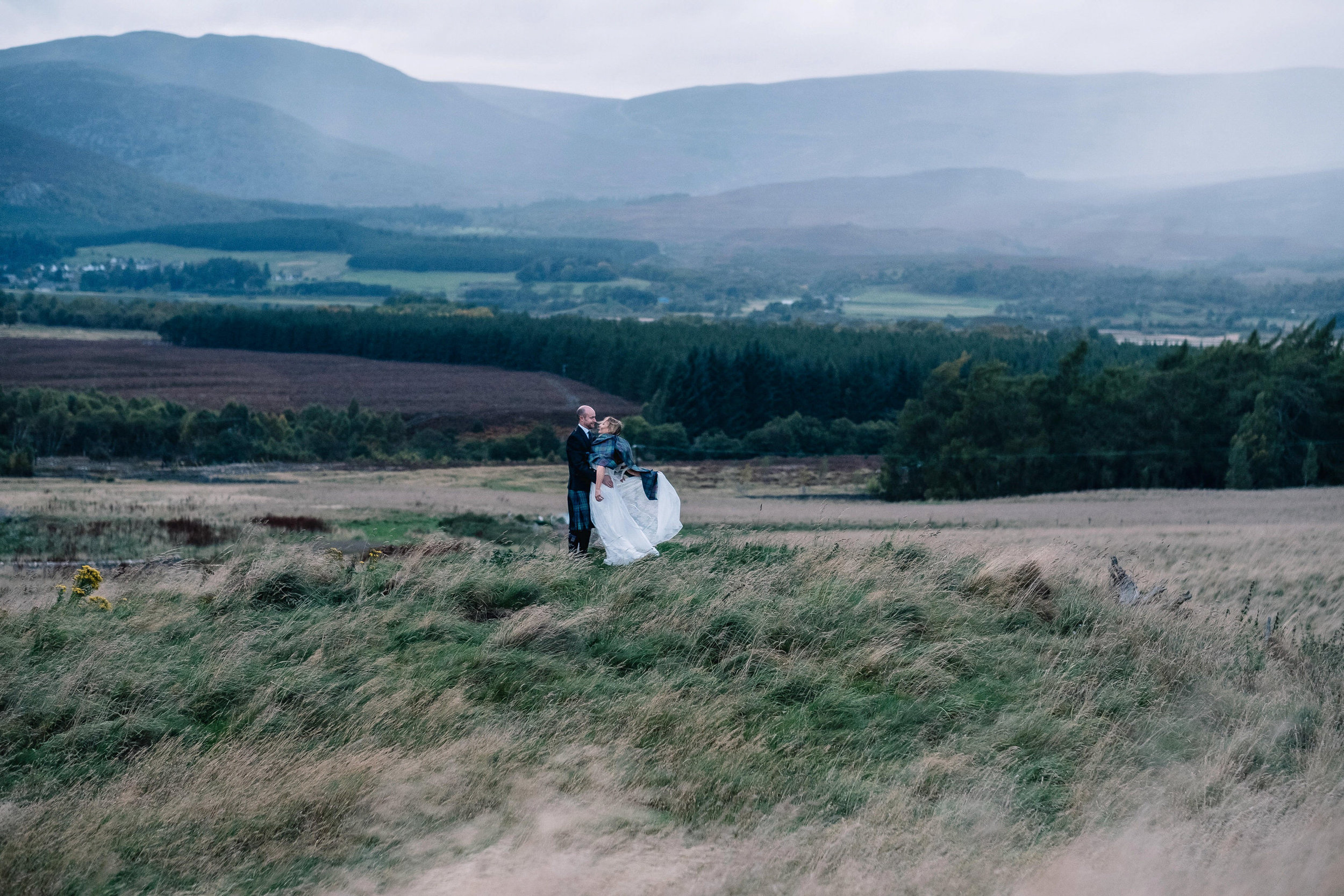  Bride and groom stand in open fields of Kingussie during their small intimate Scottish wedding 