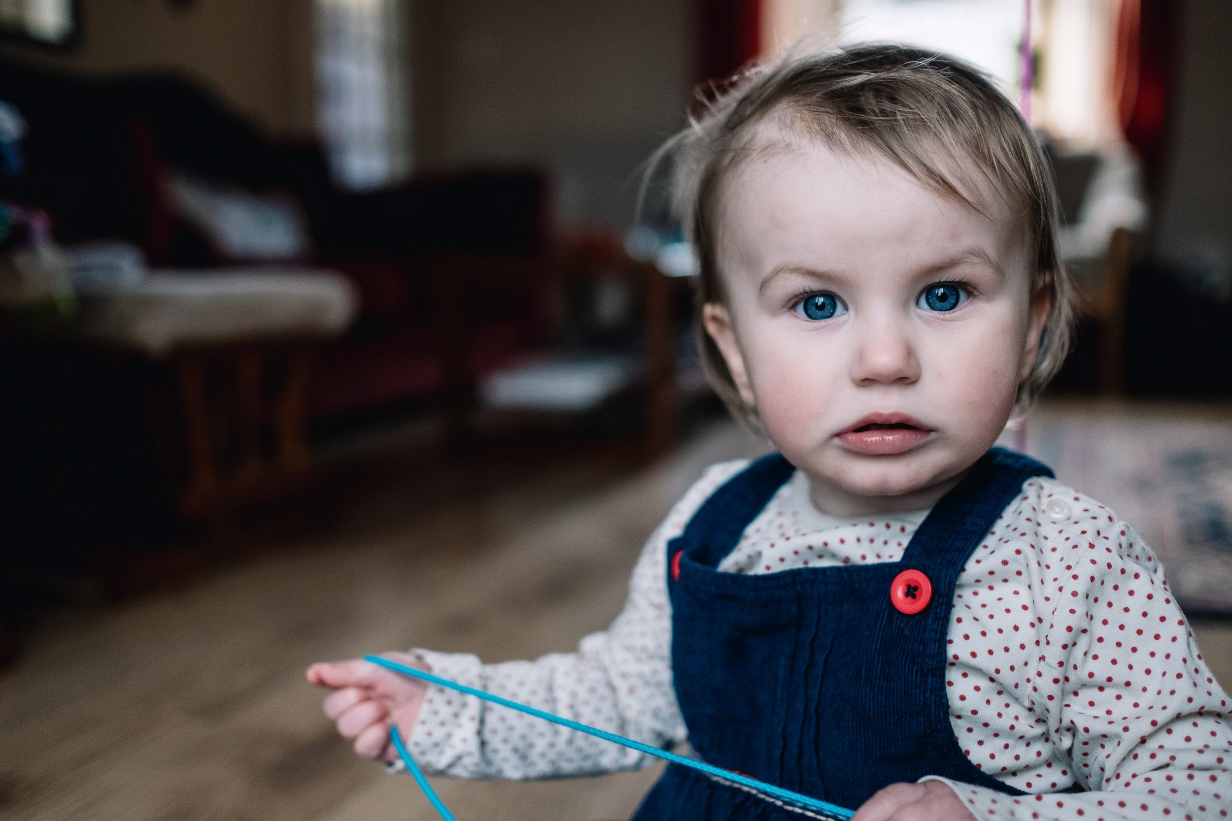 A toddler sitting in her house and looking directly to camera.