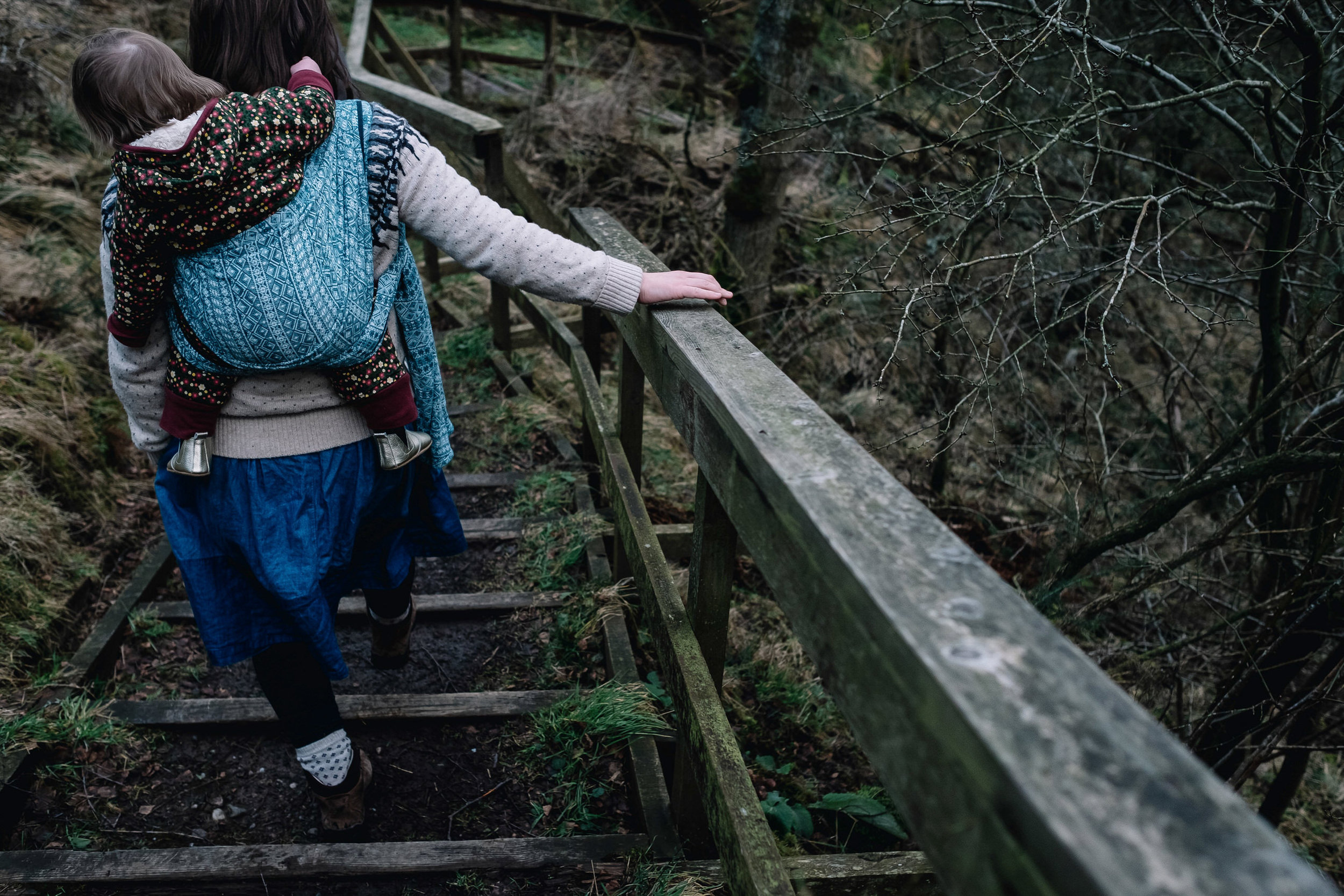 Mother holds onto wooden beam as she walks in a forrest.