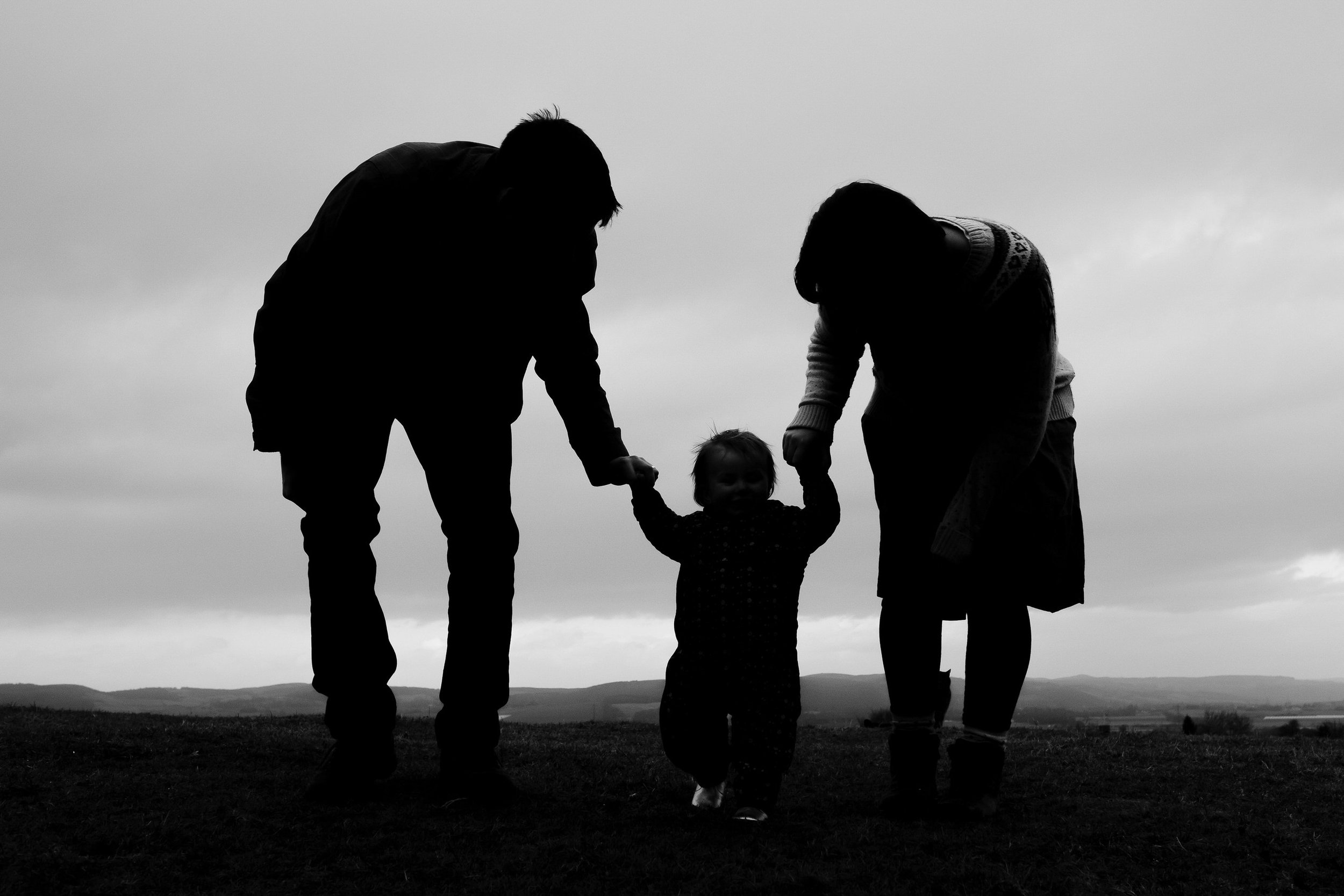 Family are silhoutted as they help their daugher to walk.