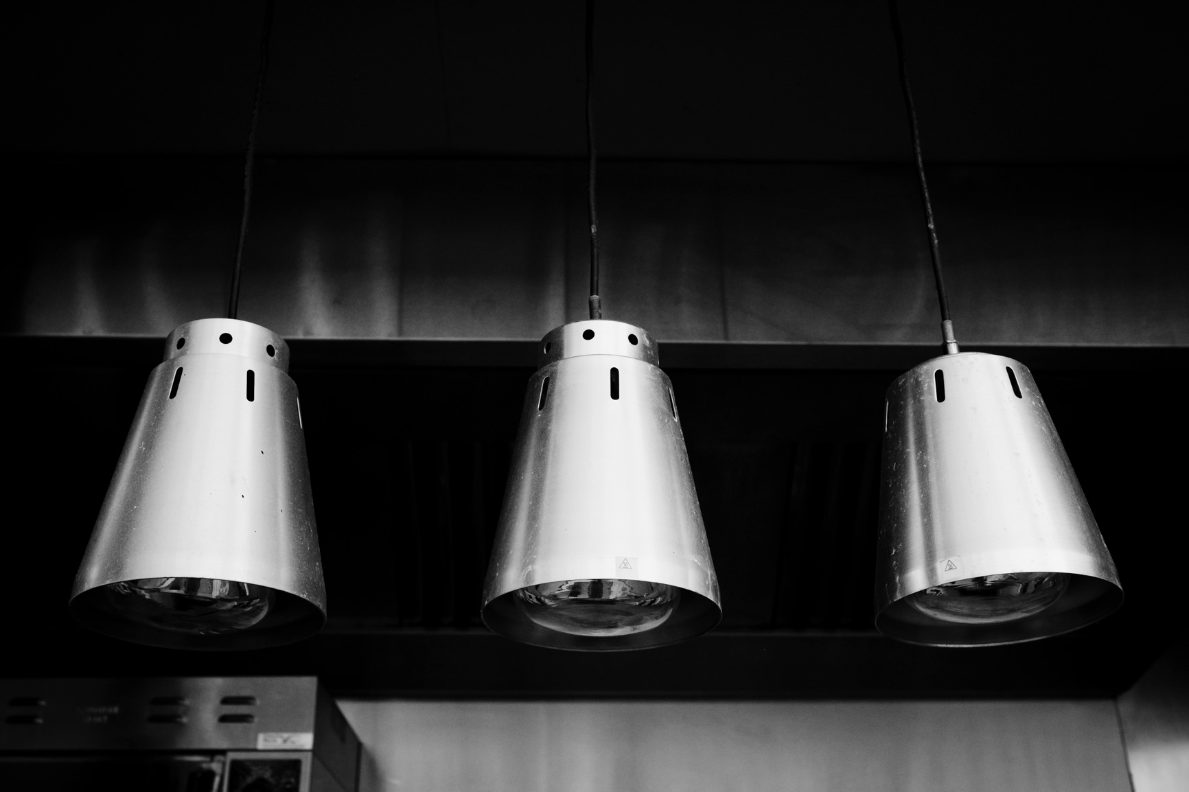 Three steel lampshades hanging from roof of outdoor area.