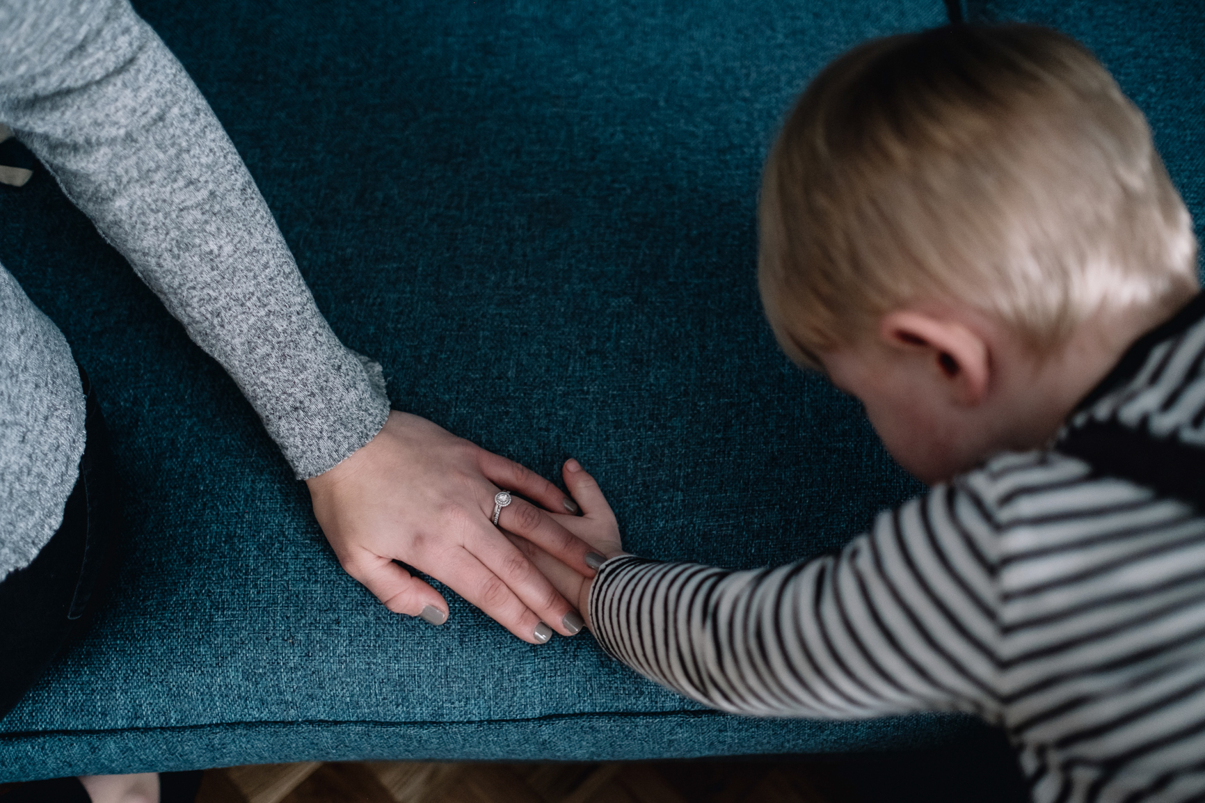  Boy's hand on blue sofa and mother's hand is on top. 