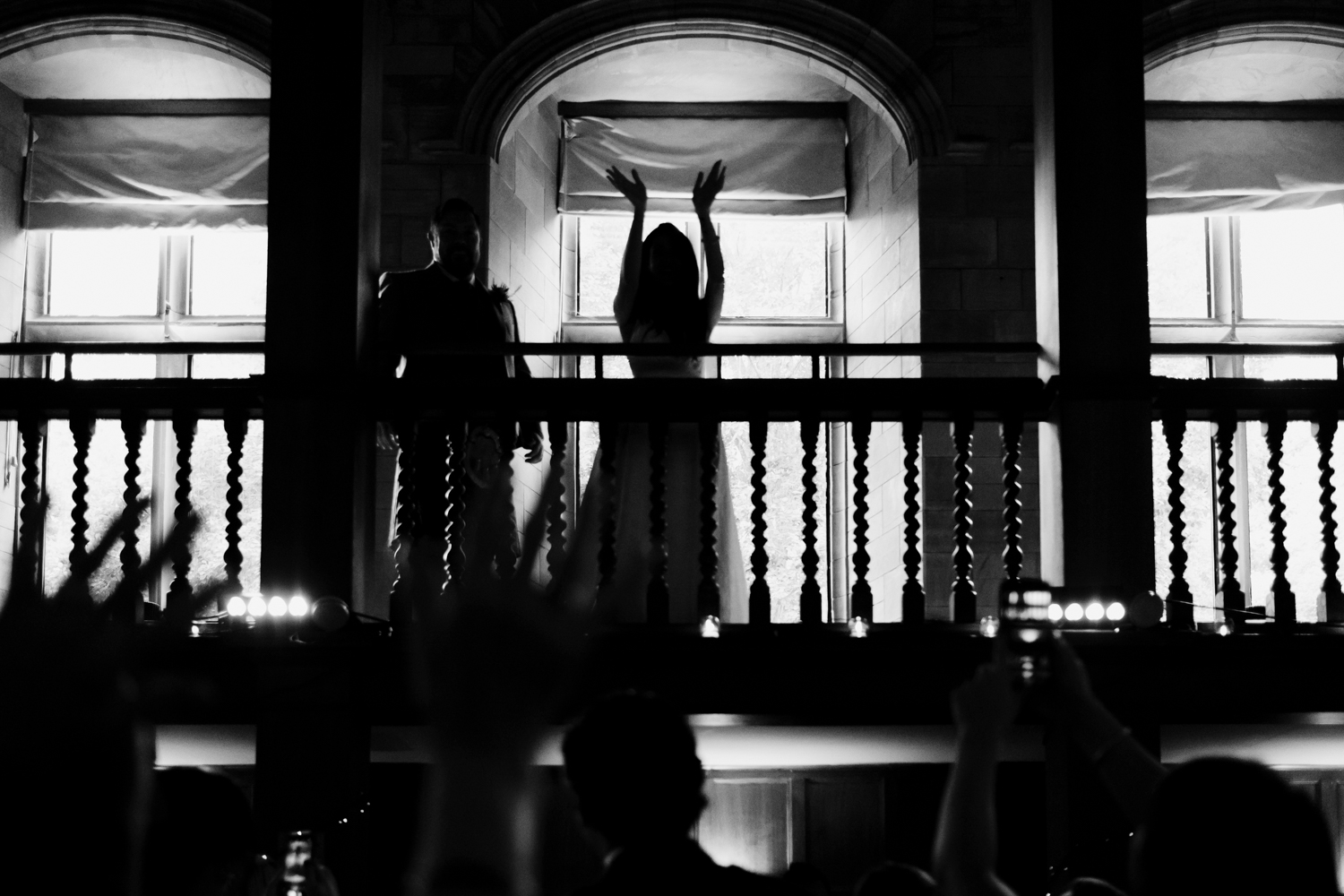  Bride holds hands up and claps from balcony of Achnagairn Estate ballroom. 