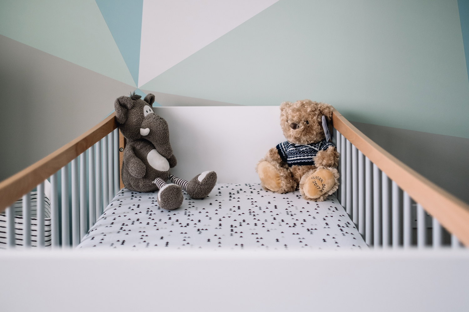 Two teddies are at the top of a baby's cot.