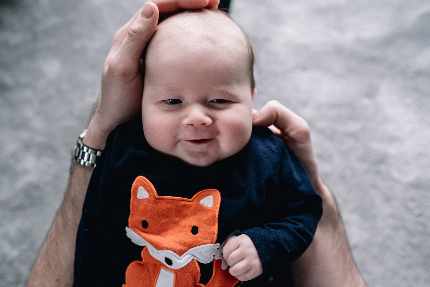 Baby being held by father is smiling directly at the camera.
