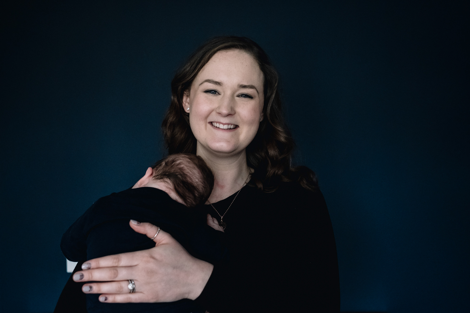 Mother holding baby and smiling directly at the camera.