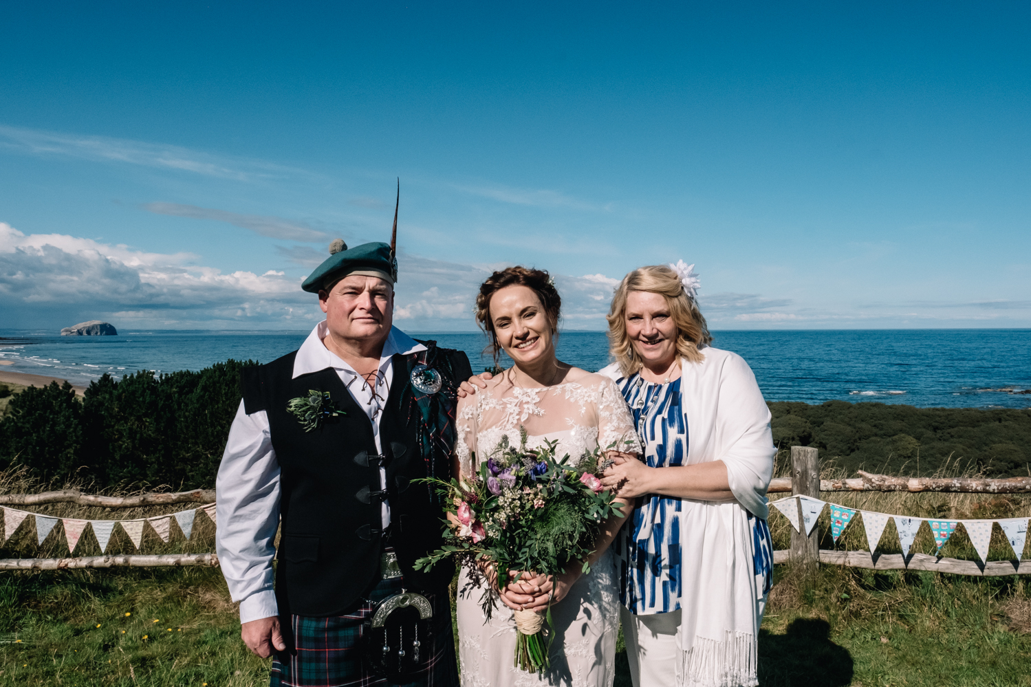 Bride stands with her parents and all are smiling.