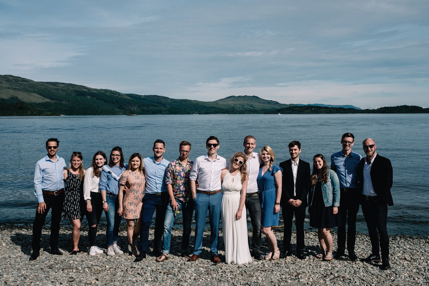 Bride and groom standing ont he shores of Loch Lomond with their close family.