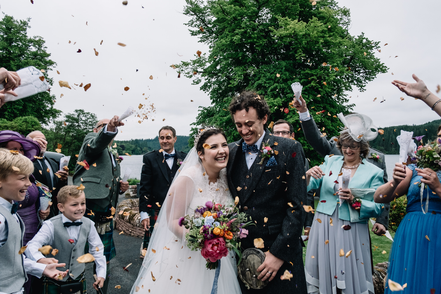  A couple are smiling + laughing as they are surrounded by their friends and family who are throwing confetti. 