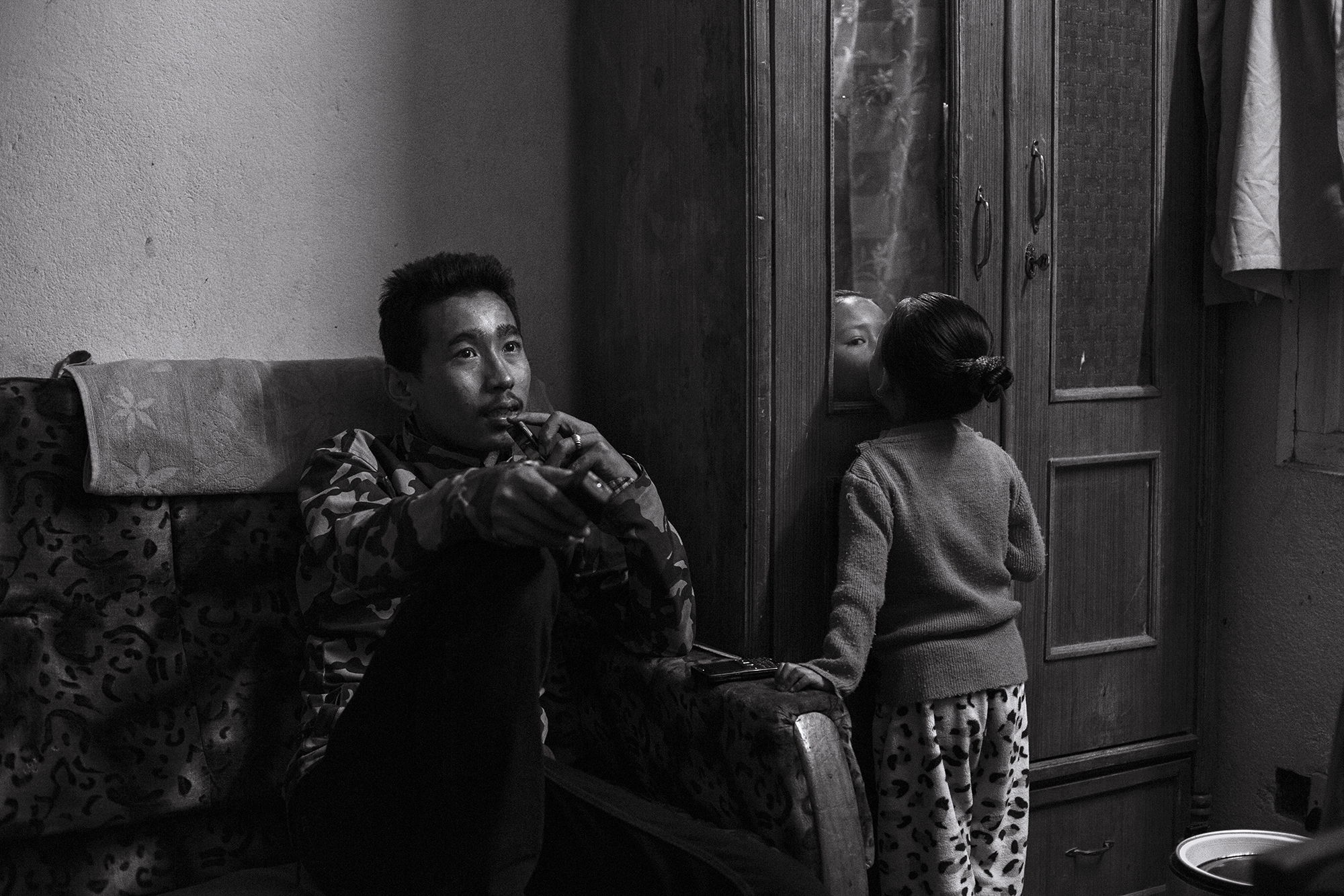 Anu's brother Anil (20) watches tv while Anjika plays. Anil works in an iron shop as a labourer. He and Anu are the sole providers for the family.