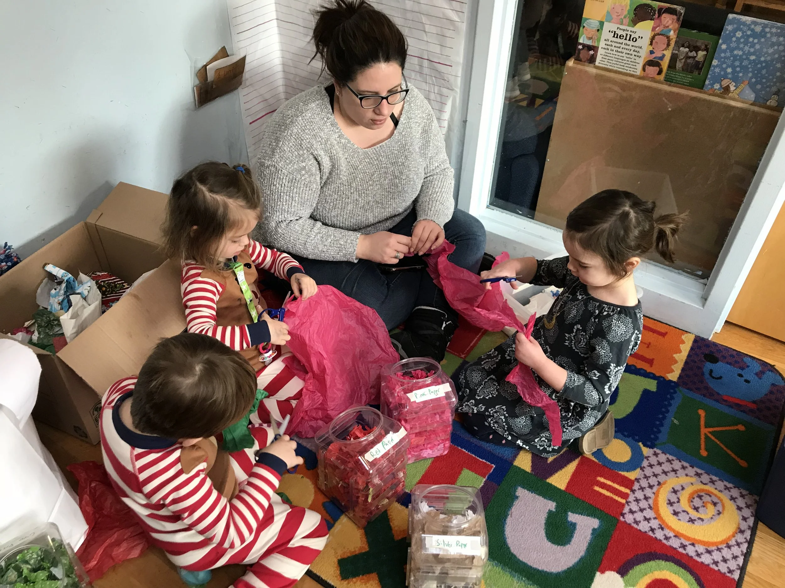 The preschoolers are cutting and sorting paper for paper making. This supports this supports children learning how to use scissors and developing small muscles.