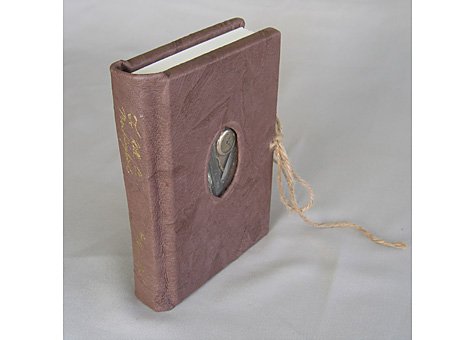 Binder: Lauren Ottariano: Harper Lee, To Kill a Mockingbird. Harper Collins Publishers, Inc., New York, NY, 1999. Leather case bound book with window, layered board, spine stamping, and tie. The leather represents tree bark, with the objects in the window being the treasures found in the hollow of a tree. The clamshell box is constructed in a different way than a standard clamshell, with two doors in front, stamping with a twine tie and lift. The different colors of the box lining represent the two skin tones of the book's main characters.