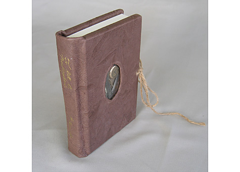  Binder: Lauren Ottariano: Harper Lee, To Kill a Mockingbird. Harper Collins Publishers, Inc., New York, NY, 1999. Leather case bound book with window, layered board, spine stamping, and tie. The leather represents tree bark, with the objects in the 