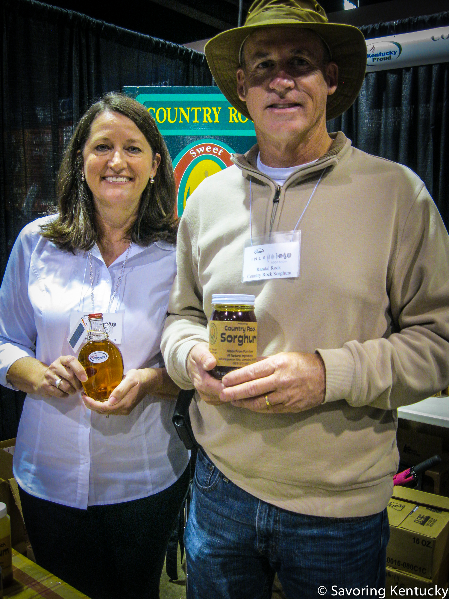 Jill Rock and Randal Rock, part of the Country Rock Sorghum enterprise. Jill holds maple syrup and Randal holds sorghum, both vintage 2014.
