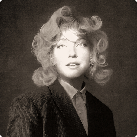 Black and white photo of a woman with curly hair wearing a suit and shirt, looking slightly to the side.
