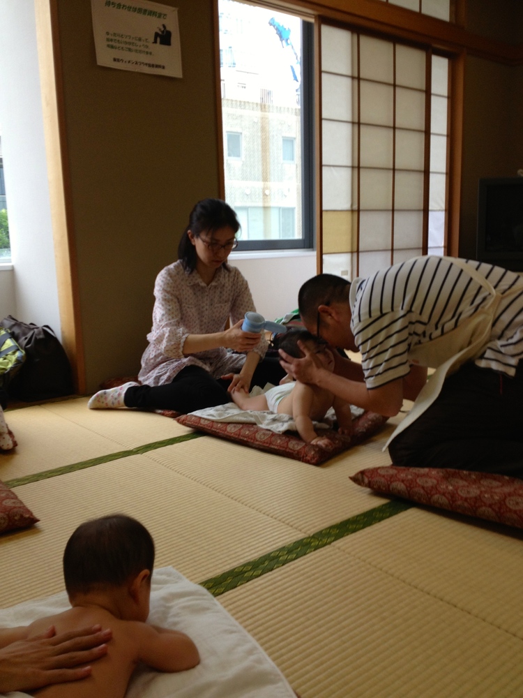 A parent trying the hairdryer technique (In lieu of moxa) while the acupuncturist teacher engages the baby