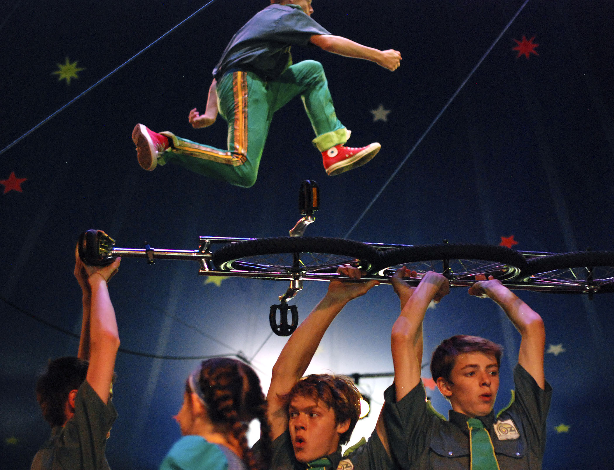 A performer jumps on a trampoline while others carry a giant unicycle across the stage during Circus Smirkus' "Oz Incorporated" in Brattleboro, Vt. on July 16, 2013.