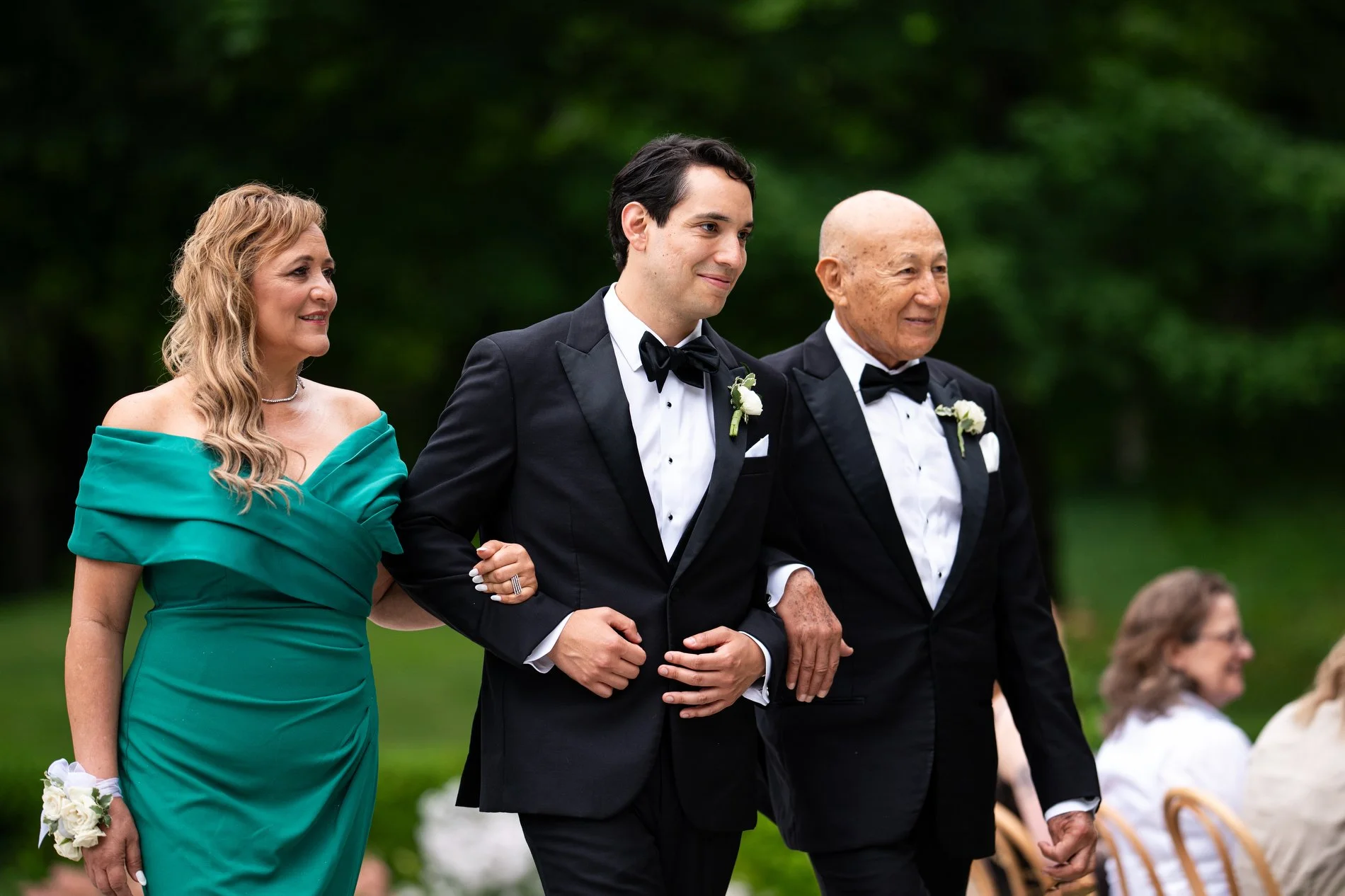 A groom walks down a long aisle with his parents during his romantic Berkshires microwedding ceremony in the French garden at The Mount.