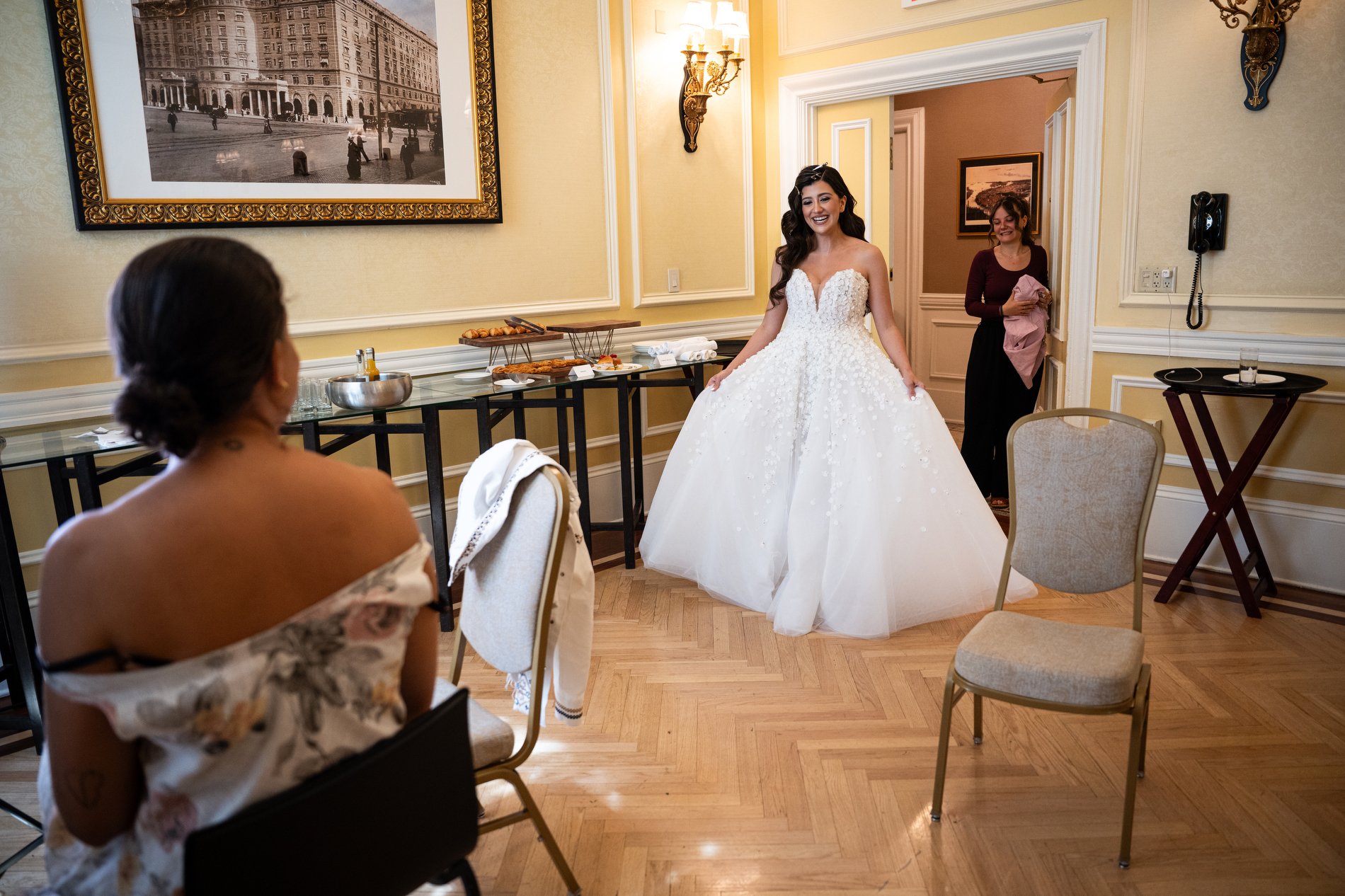 A bride shows her friend her wedding gown after getting dressed during her Boston hotel wedding at Fairmont Copley Plaza.