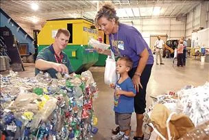 Staff Photo by Tim Barber: Michael Foxx, right, Recycling Center operations manager at the Dalton-Whitfield Regional Solid Waste Management Authority, punctures a plastic bottle as Matthew Ryerson, 3, and North Whitfield Middle School teacher Jill Ryerson listen for air to be released at recent open house.