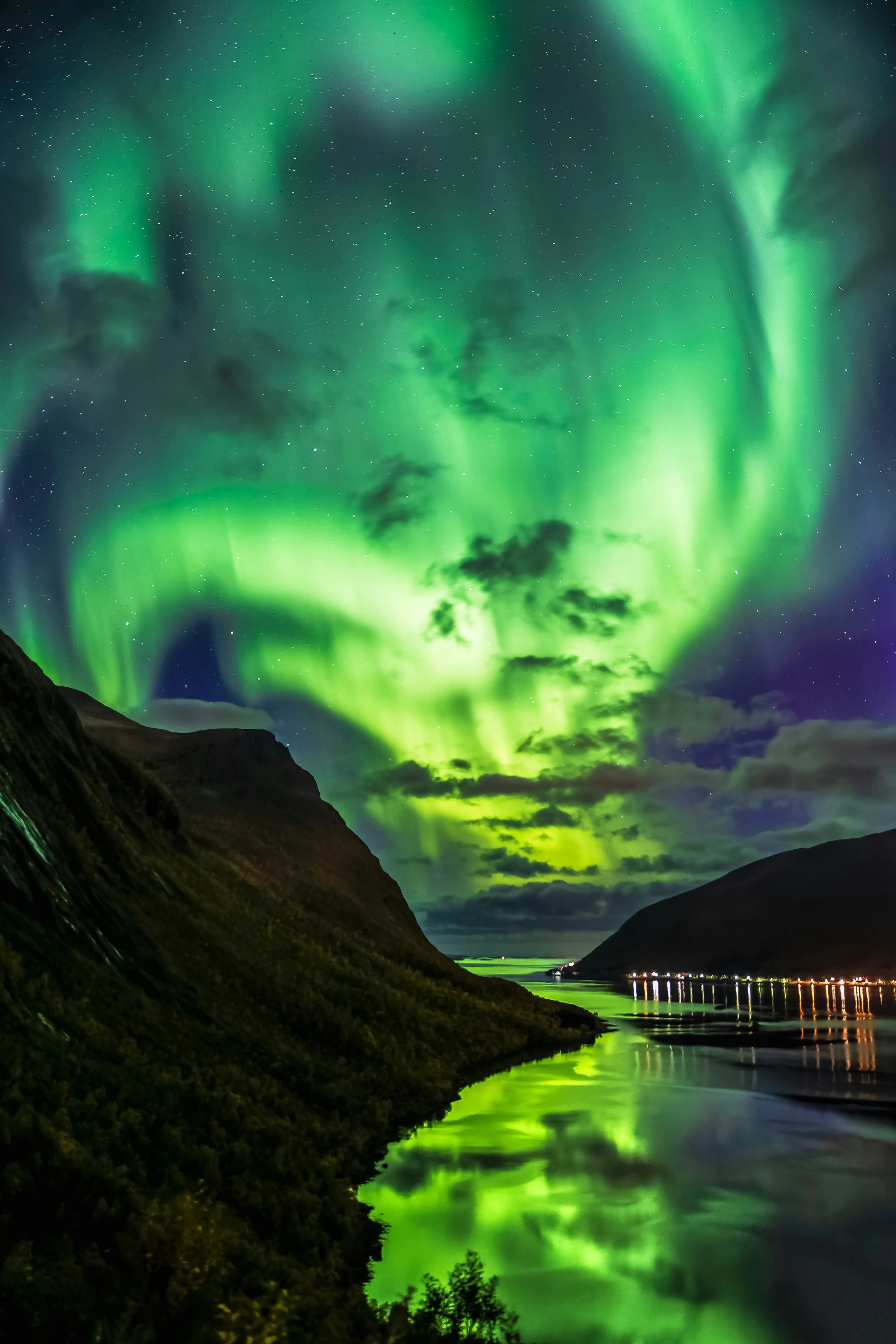 Northern Lights illuminating the night sky over a mountainous landscape with a body of water reflecting the lights.