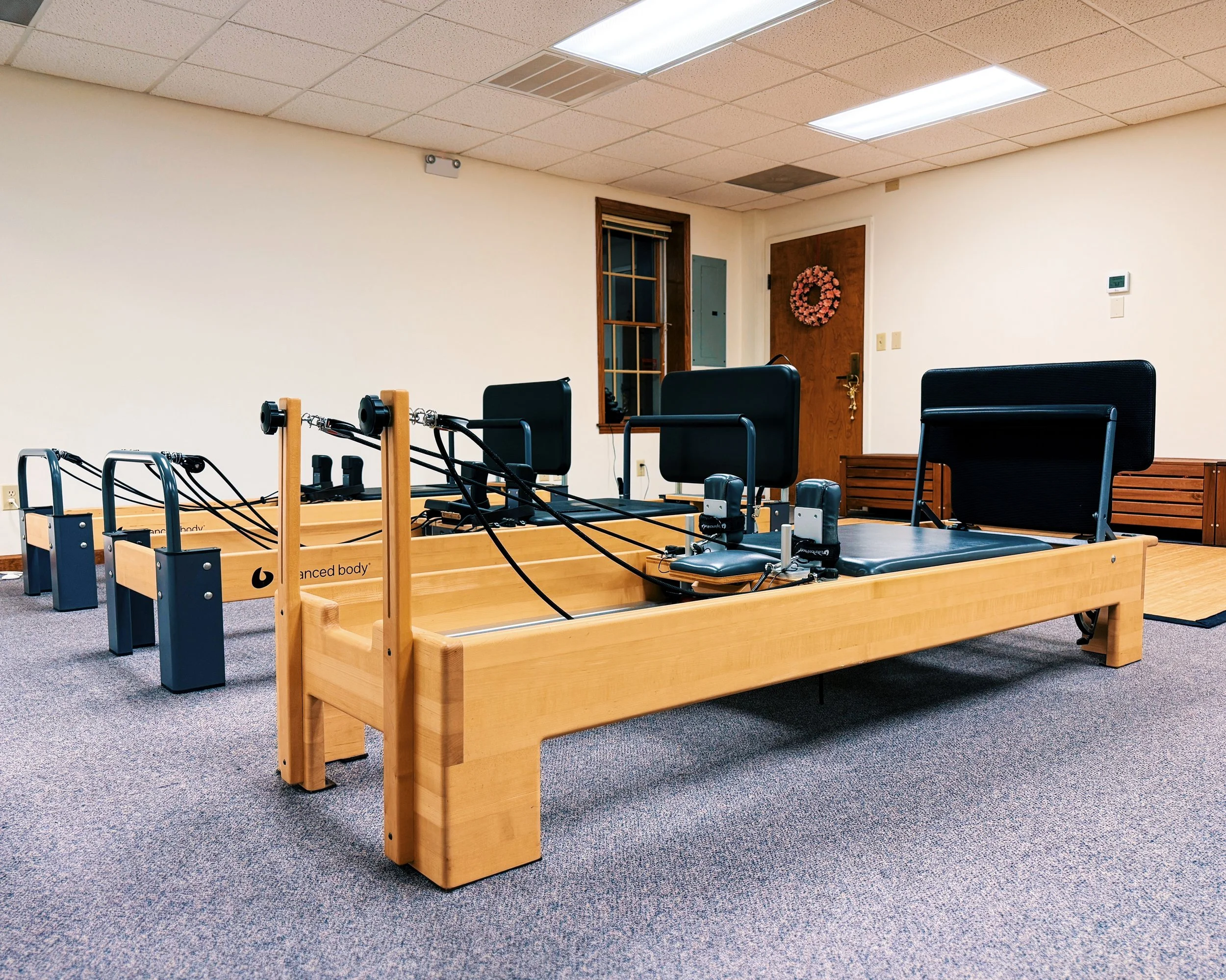 A physical therapy reformer machine in a treatment room, with adjustable black cushioned headrests and foot straps