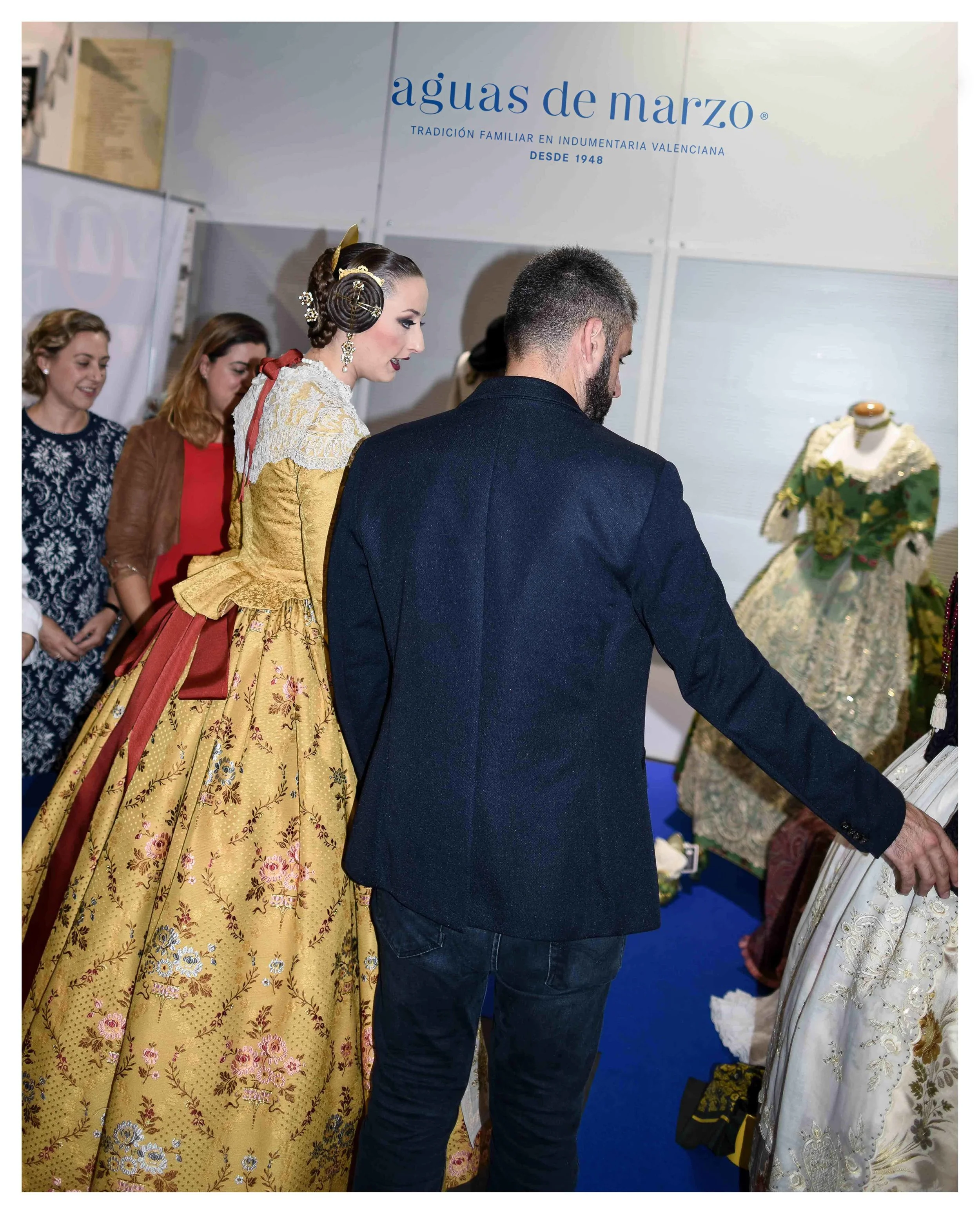 En la imagen, en primer plano la Fallera Mayor de Valencia 2018, señorita María del Rocío Gil Uncio, y D. Pere Fuset comentando sobre las propuestas del stand de Aguas de Marzo indumentaria. Al fondo María y Fátima Aguas de Aguas de Marzo indumentaria.