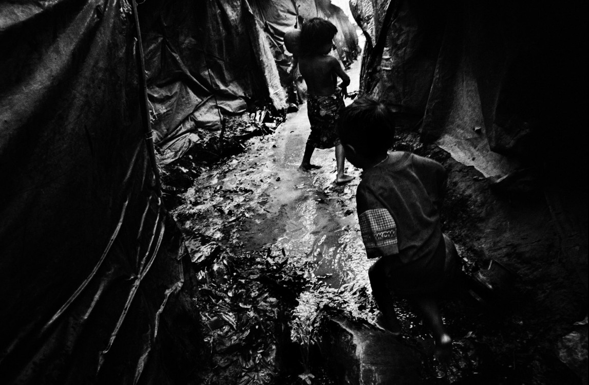  Deux enfants jouent dans une allée inondée du camp de Tal. Chaque année, pendant la mousson, l'eau qui vient des collines qui entourent le camp se mêle à celle des égouts, et y déverse immondices, carcasses, débris. (2006)  © Greg Constantine,&nbsp;