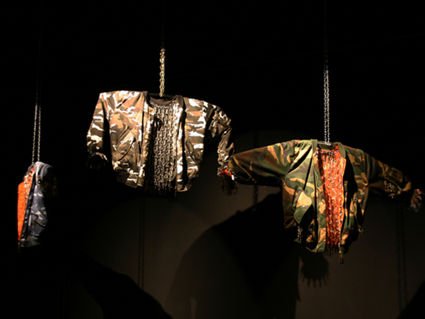 Passeur #1, #2, #3, 2012. 3 Bombers de l'armée, clés, moteurs, chaînes. 300 x 150 x 250 cm Trois bombers rebrodés d'une multitude de clés tournent à 360° tel des gardes sur leur mirador. Ils semblent scruter, fouiller la salle à la recherche de suspects. Ces fantomes détiennent les clés au double sens du terme, symboliquement les clés de la compréhension. Certains savent, gardent des informations, les distribuent aux compte-gouttes ou les détournent.... Mais aussi les clés qui ouvrent les portes des frontières, celles des réseaux de passeurs.